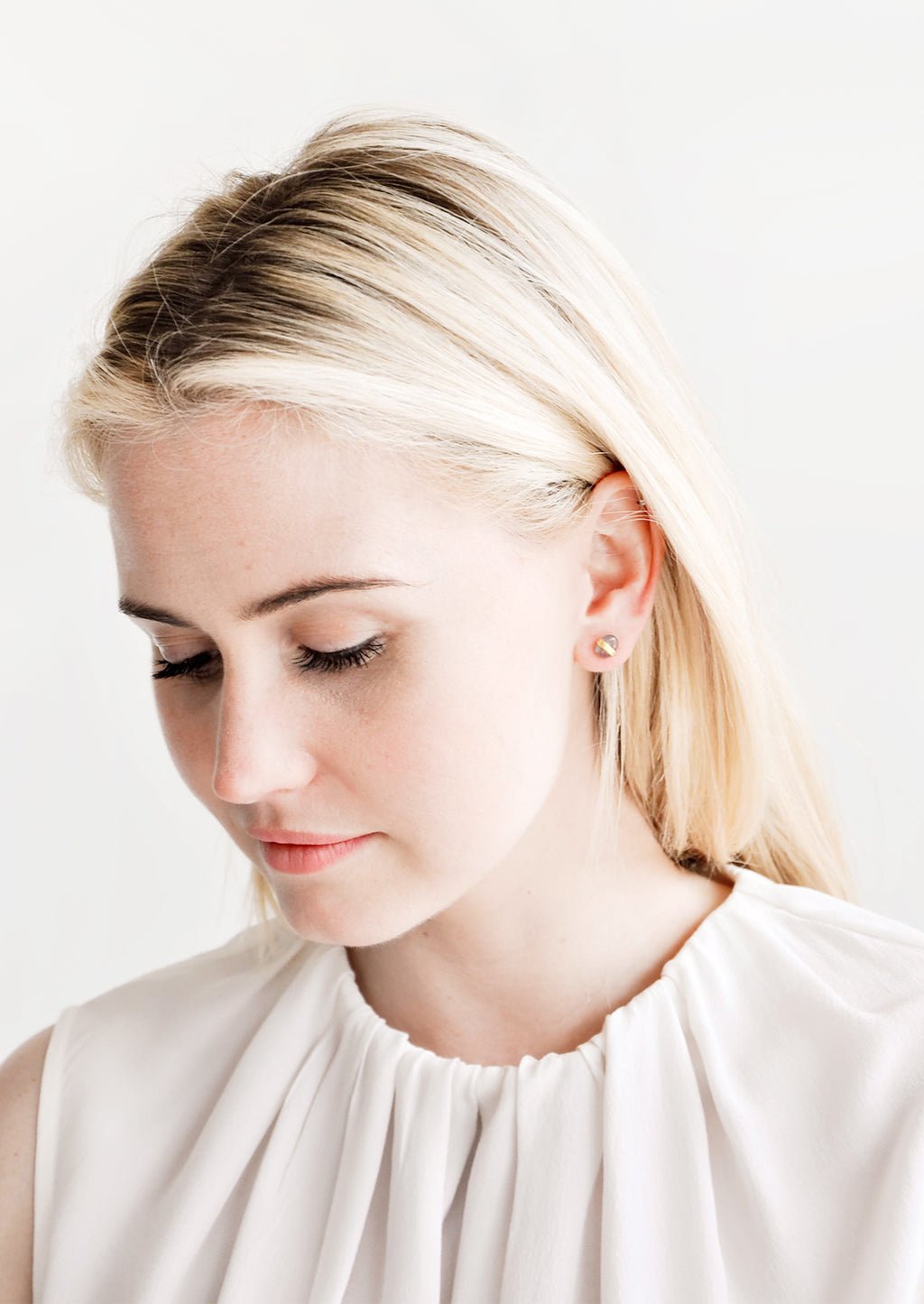 2: Blonde model looking down, wearing silky white blouse and pebble stud earrings.