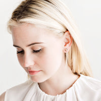 2: Blonde model looking down, wearing silky white blouse and pebble stud earrings.