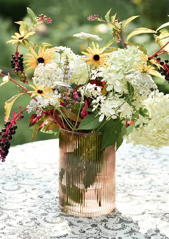 A ribbed peach glass vase with floral arrangement.