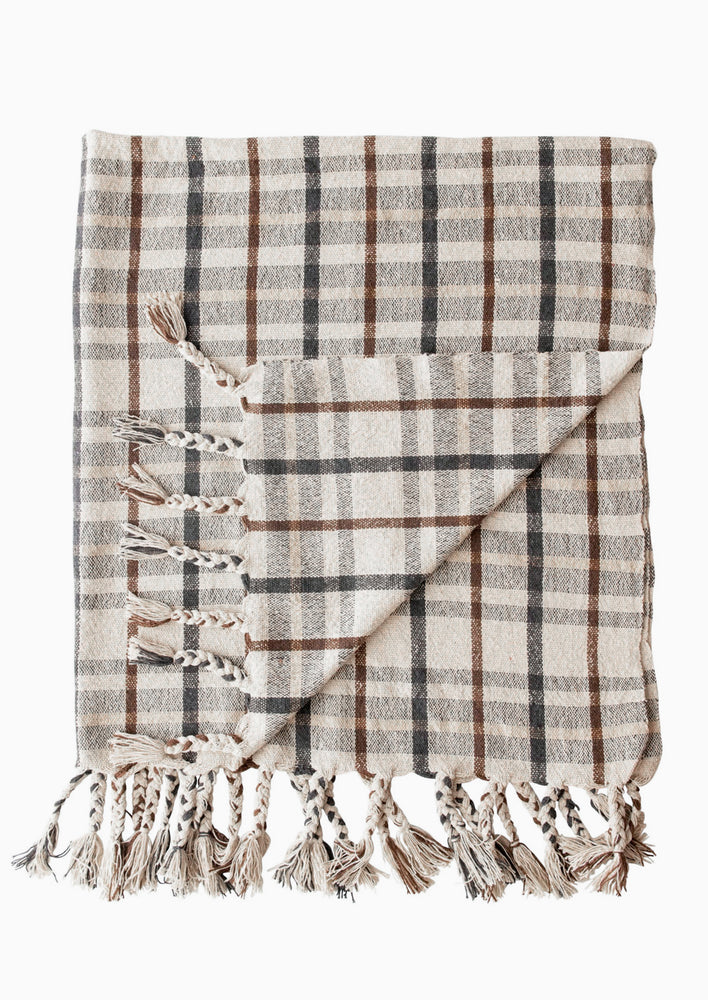 A throw blanket in cream with black, beige and brown plaid pattern.