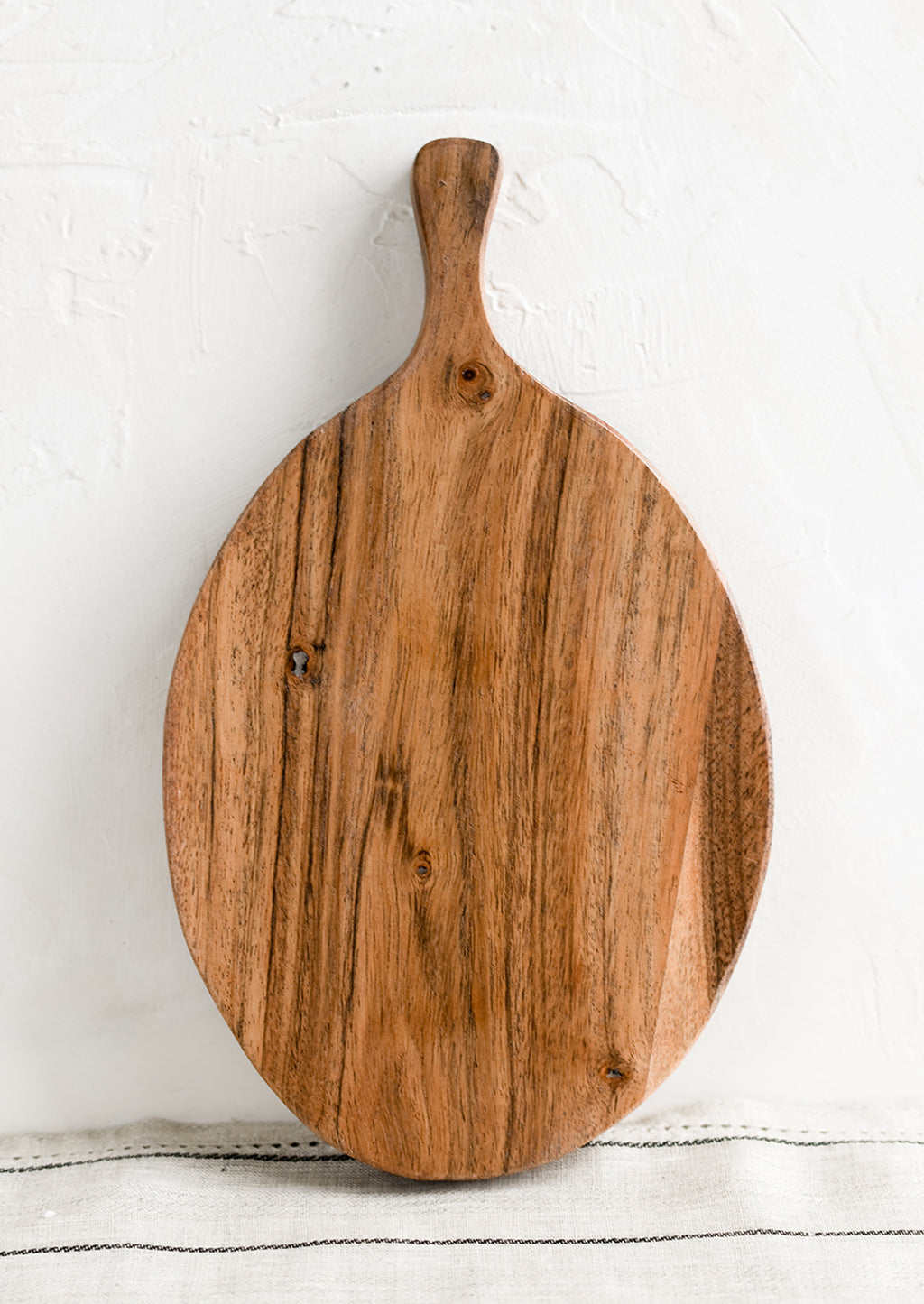 1: An oval shaped paddle-style cutting board in acacia wood.