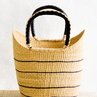 1: Winged tote basket made from natural elephant grass with thin black stripes. Woven black and natural leather handles at top.