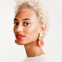 2: Model wears orange and gold earrings with white top.