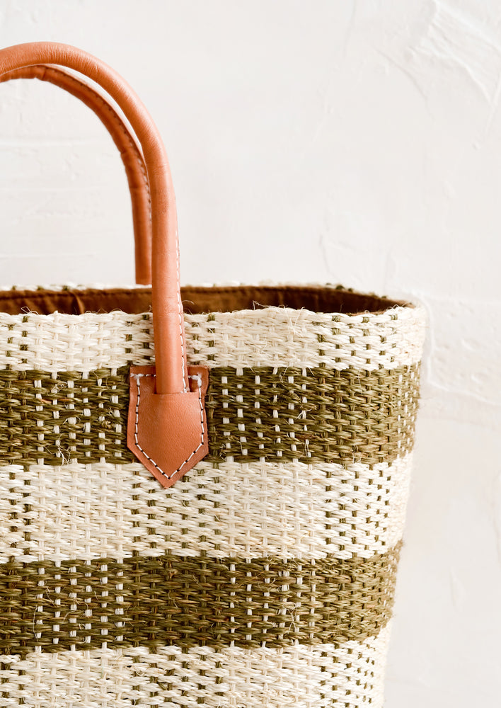 A raffia tote with natural leather handle and white stitching.