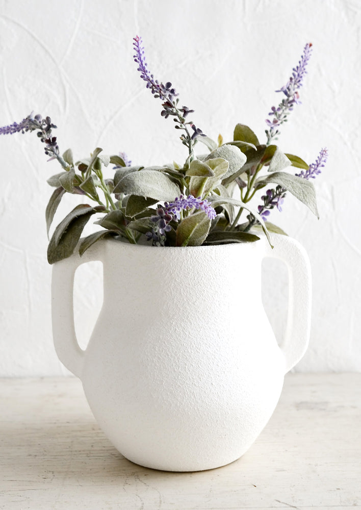 A matte white ceramic vase with lavender sprigs.