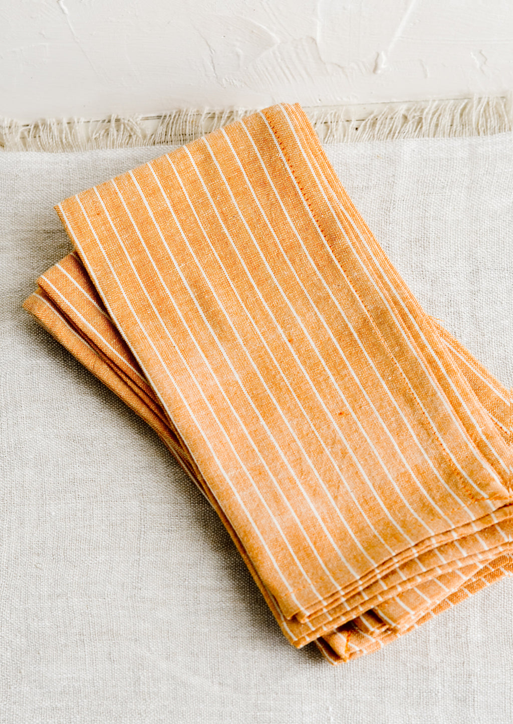 1: Folded fabric napkins in a pile featuring orange and white pinstripe pattern.