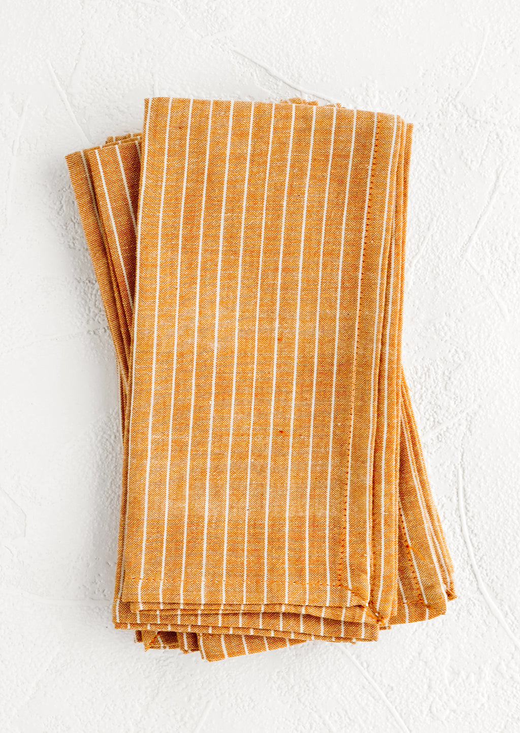 2: Folded fabric napkins in a pile featuring orange and white pinstripe pattern.