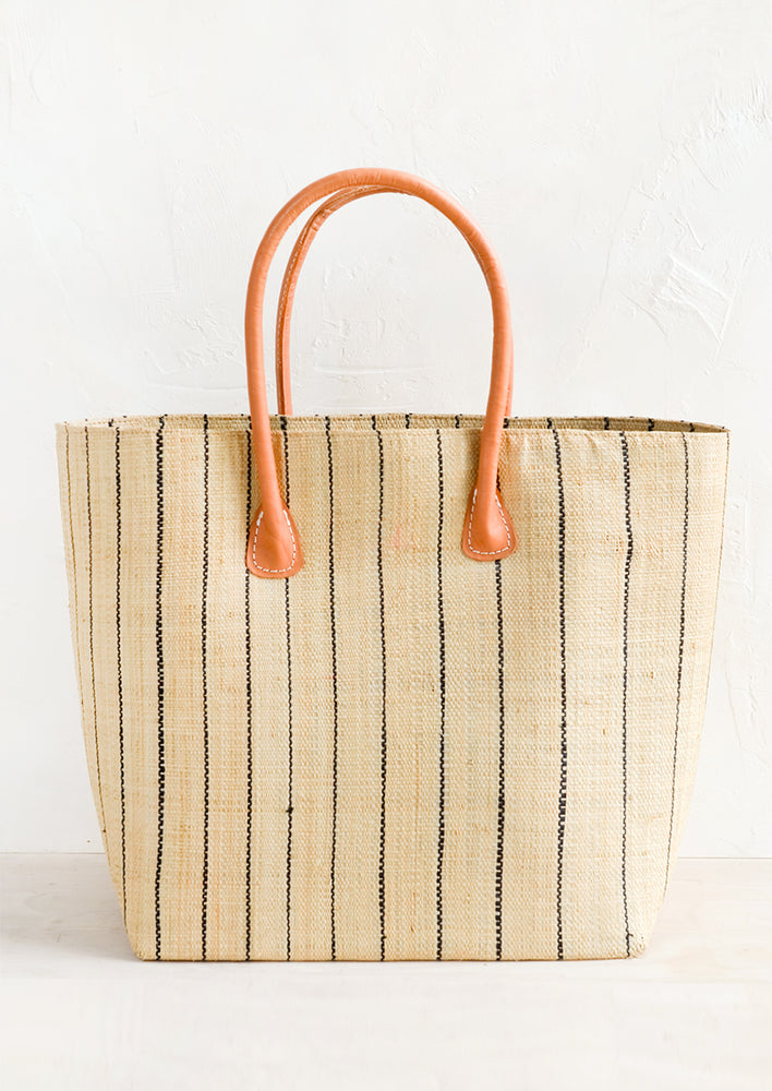 A natural raffia tote bag with thin black pinstripe pattern and natural leather handles.