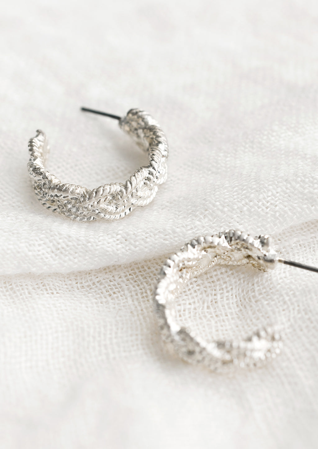2: A pair of silver-tone hoop earrings with braided texture.