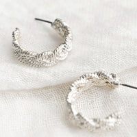 2: A pair of silver-tone hoop earrings with braided texture.