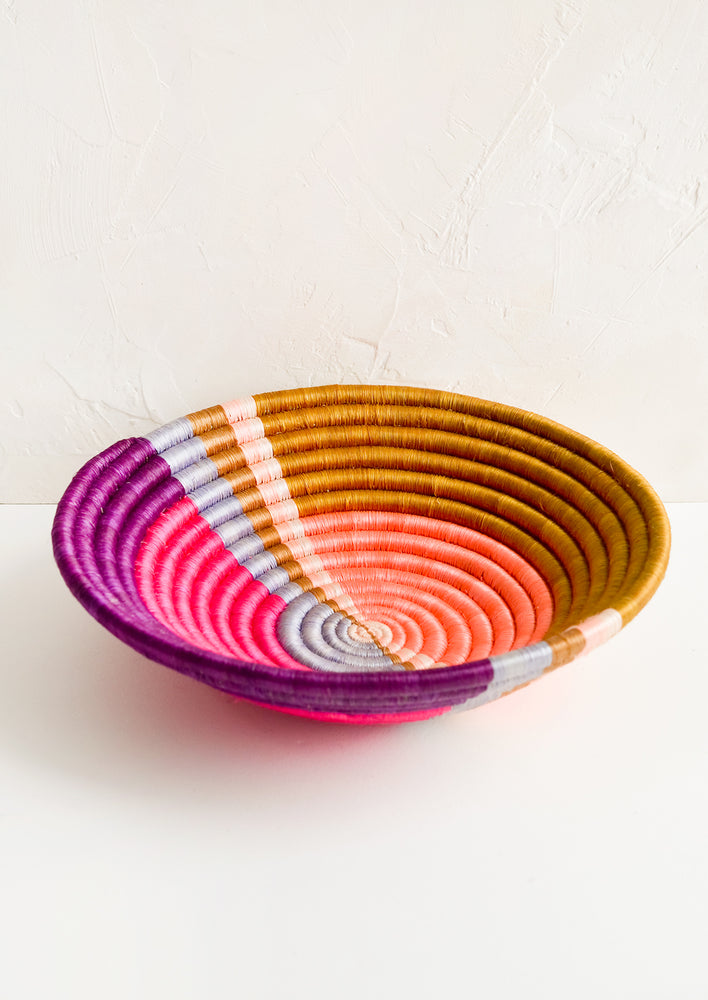 A round colorful woven sweetgrass basket with multicolor sunset design.
