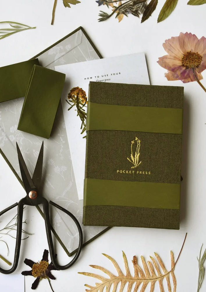 1: A green linen covered pocket-sized flower press booklet.