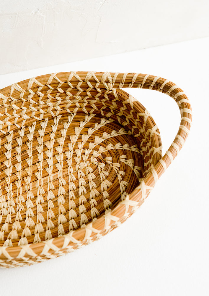 A shallow, oval shaped basket with handles at sides.