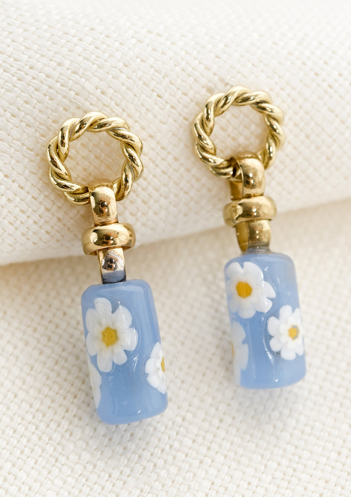 A pair of earrings with circular braided brass post and blue floral glass bead.