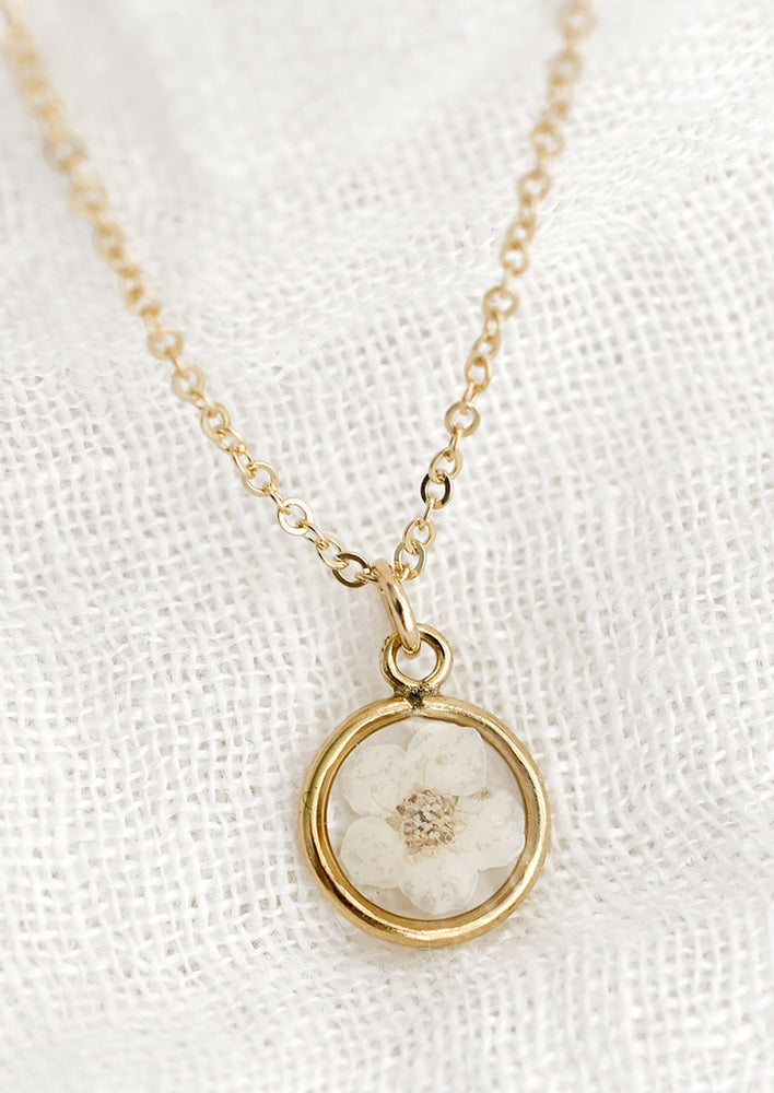 A gold necklace with a dried floral pendant set in resin