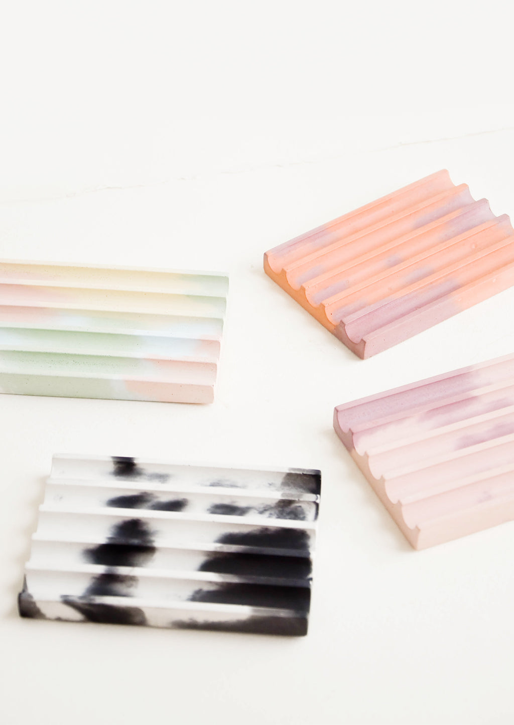 2: Four smooth concrete ridged soap dishes in rainbow, coral, pink, and black and white.