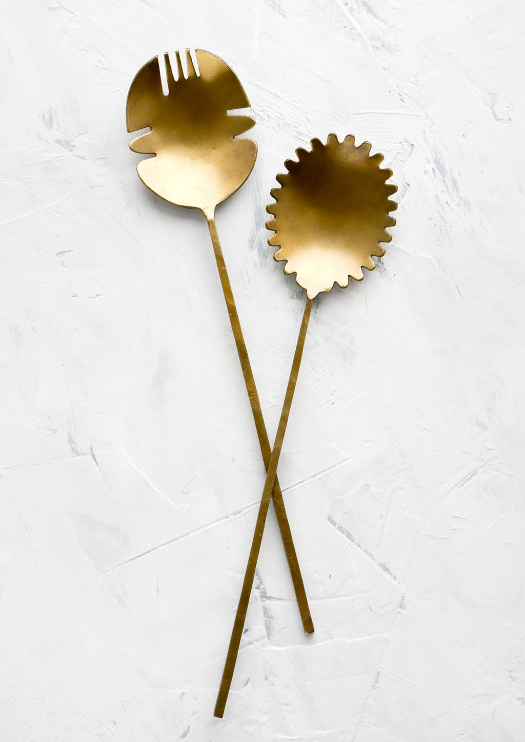 2: A pair of salad servers made from antiqued brass, shaped in a prehistoric-inspired design with slender handles.