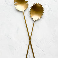 2: A pair of salad servers made from antiqued brass, shaped in a prehistoric-inspired design with slender handles.