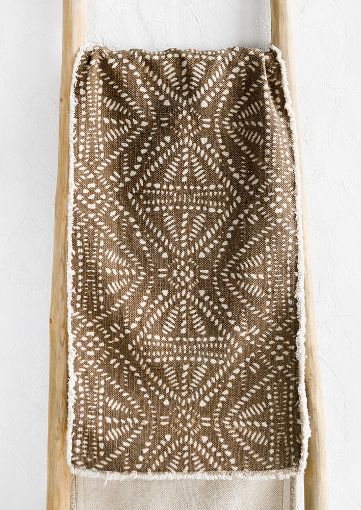 A brown canvas table runner with white resist pattern.