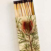 2: A matchbox with botanical protea print and brown-tipped long matches.