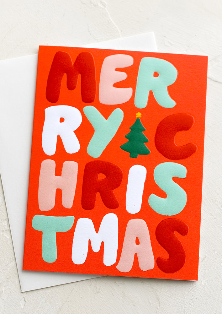 A red card with red, white and green raised lettering reading "Merry Christmas".