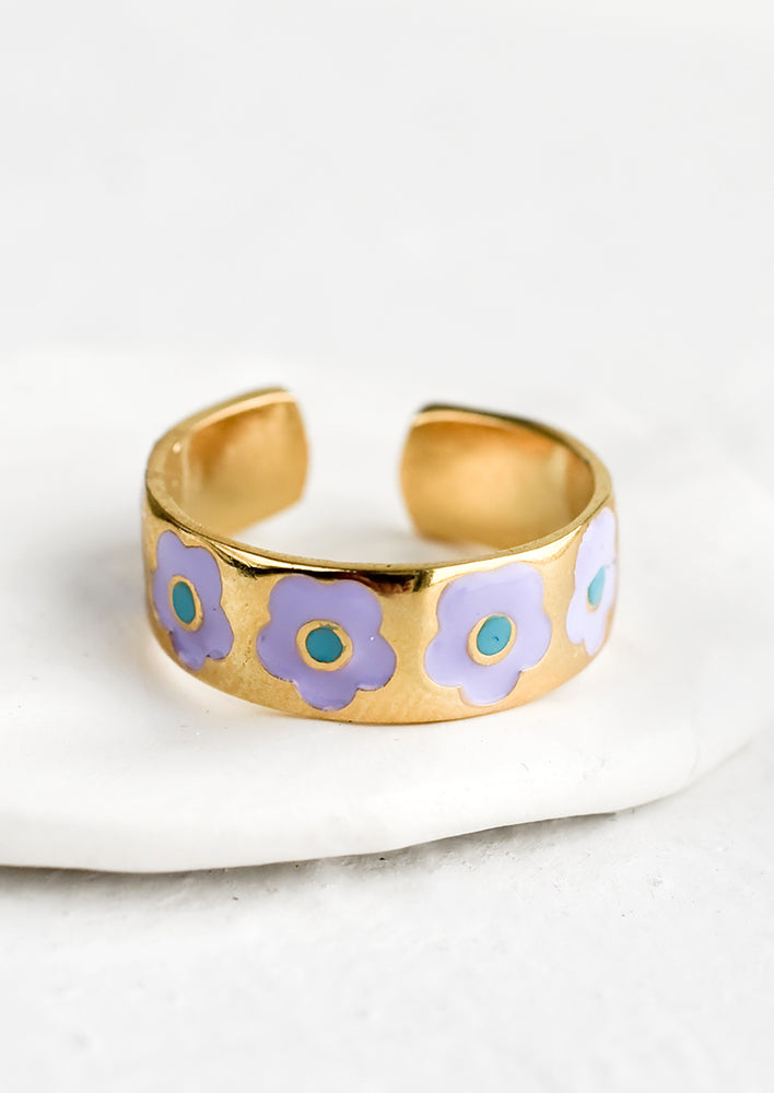 An open ended gold ring with enameled purple and teal daisy pattern.