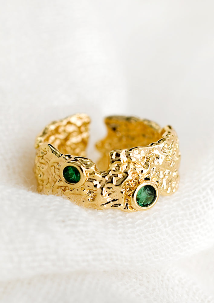 A textured gold wide band ring with two green emerald detail.