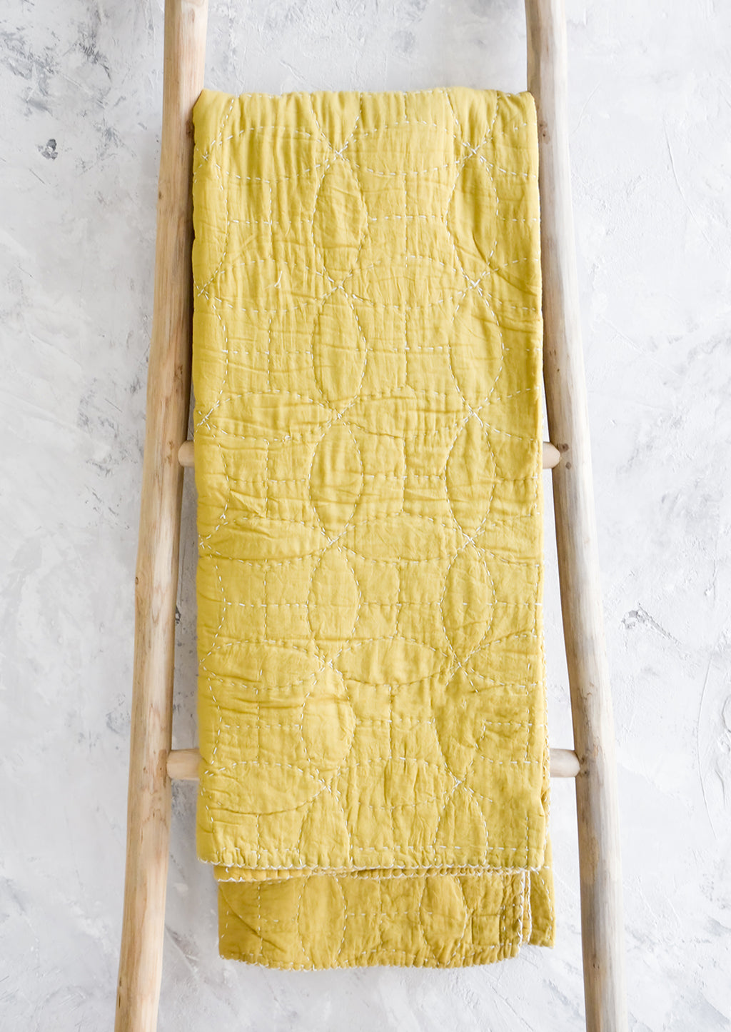Chartreuse: Chartreuse colored cotton throw with overlapping circle patterned embroidery, hanging on display ladder