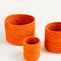 Extra Small / Orange: Set of round catchall baskets made from orange raffia in three incremental sizes.