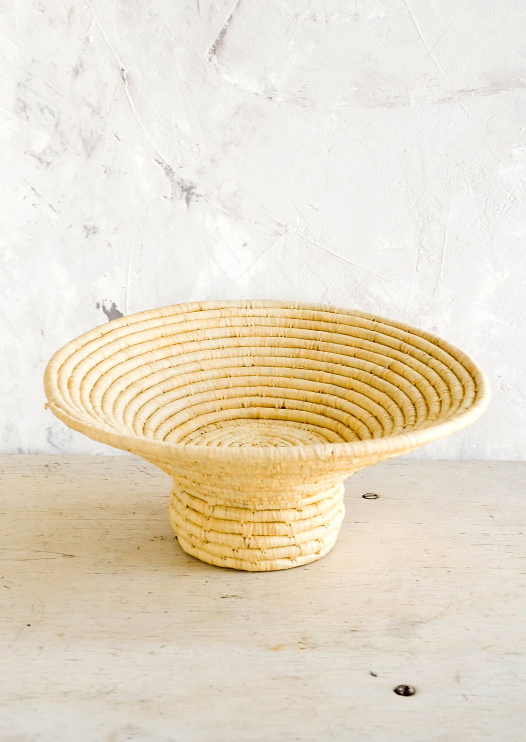 3: Footed pedestal bowl made from natural woven raffia, sitting on a table