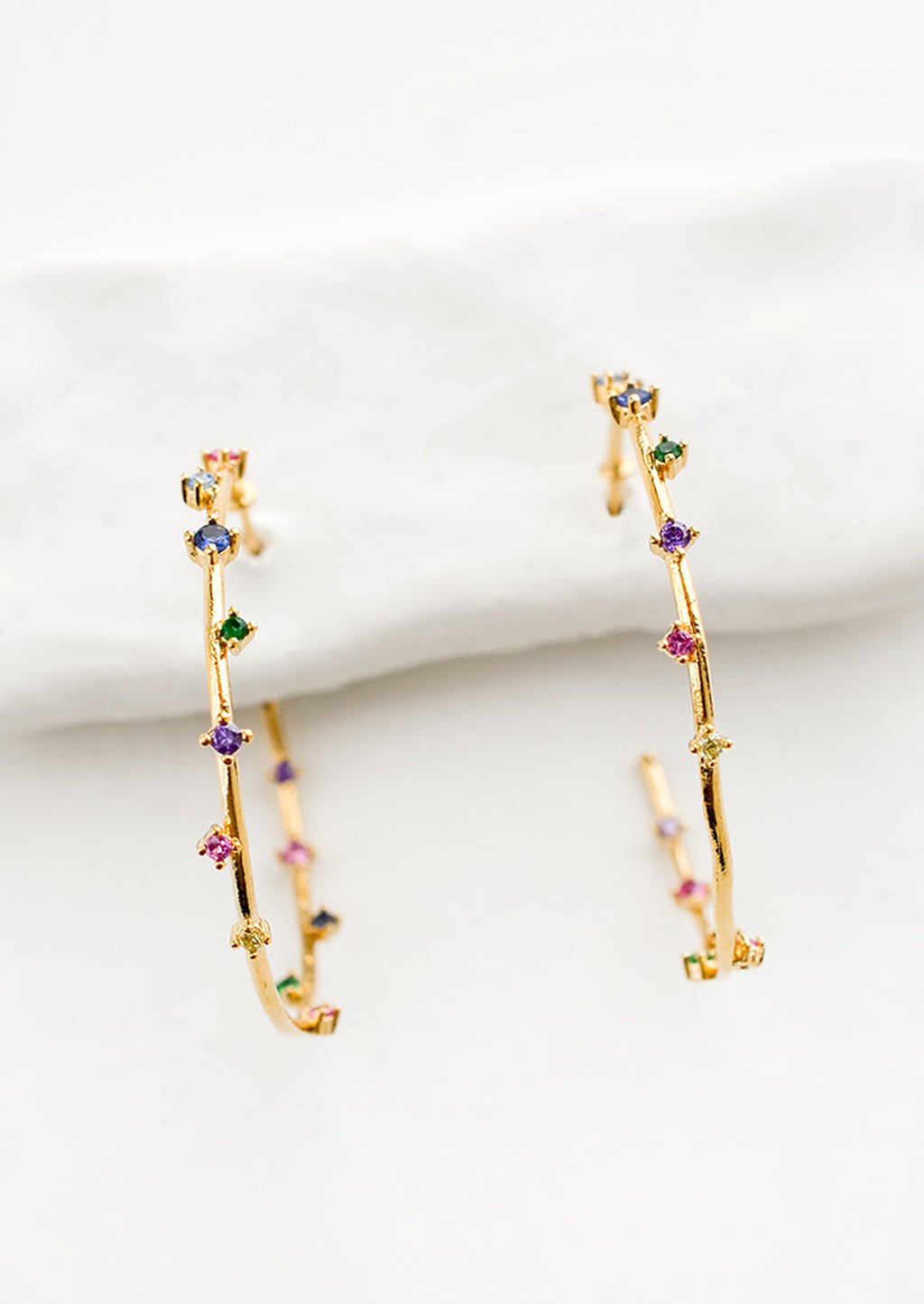 1: A pair of gold hoop earrings with colored crystals wrapping around the hoop sporadically.