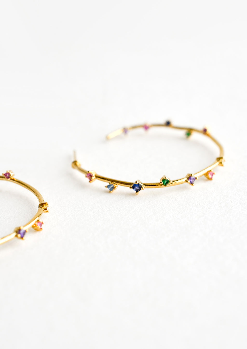 2: A pair of gold hoop earrings with colored crystals wrapping around the hoop sporadically.