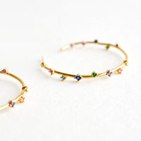 2: A pair of gold hoop earrings with colored crystals wrapping around the hoop sporadically.