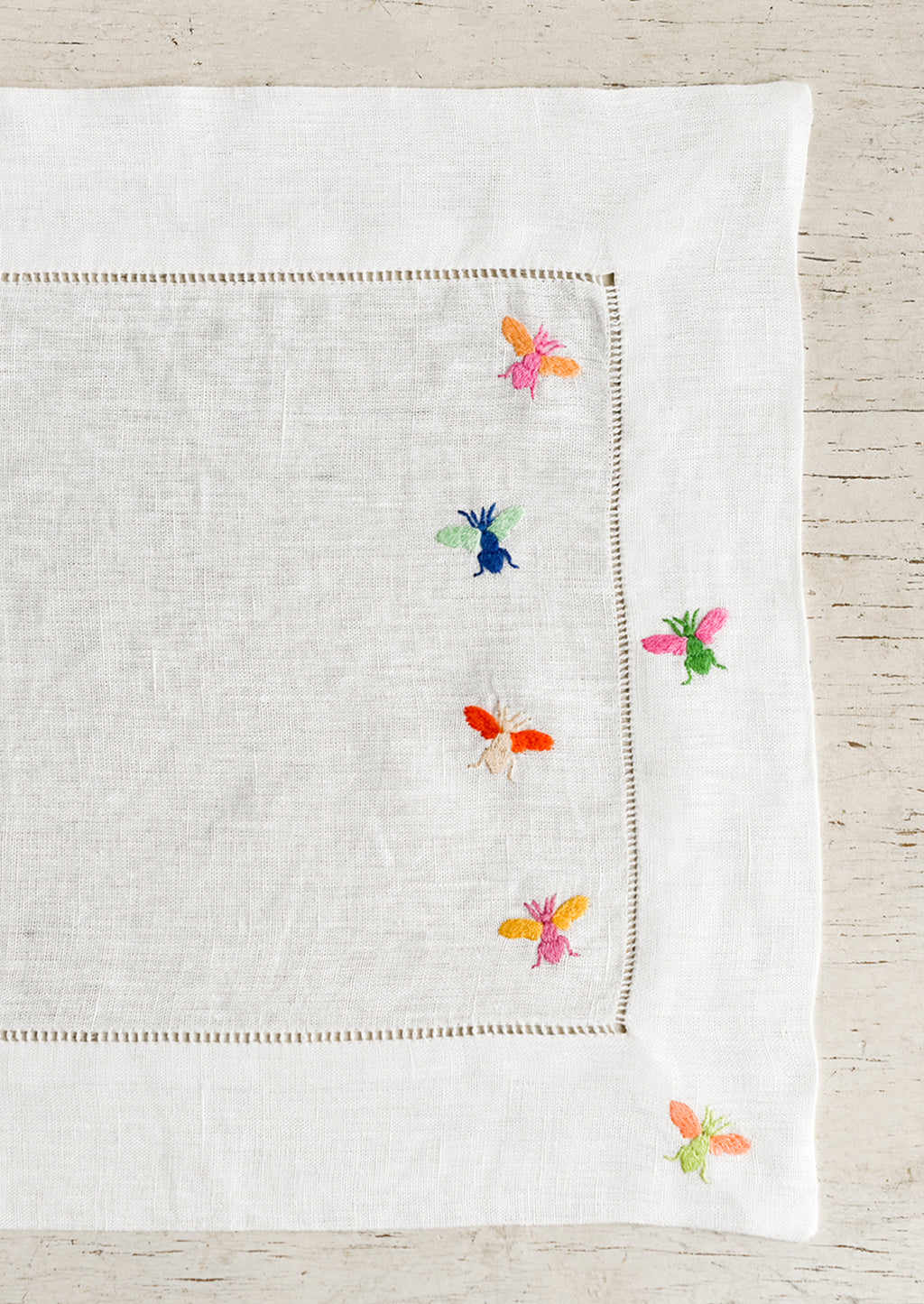 1: A white linen placemat with multicolor bee embroidery.