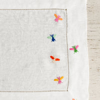1: A white linen placemat with multicolor bee embroidery.