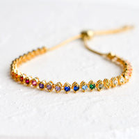 2: A gold, tennis style bracelet with marquis shaped crystals in rainbow color span.