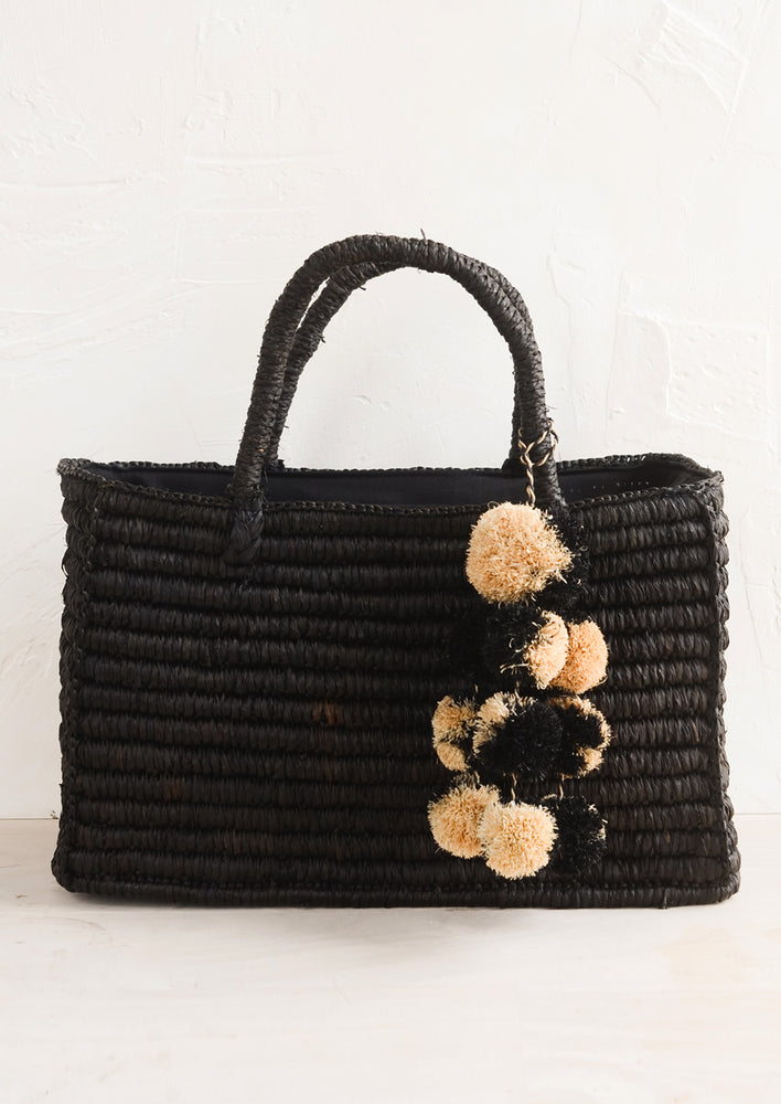 Black: An east-west raffia tote in black with straw pom pom detailing.