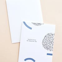 1: White notecard with black and blue geometric decoration and the text "You're doing an amazing job", with white envelope.