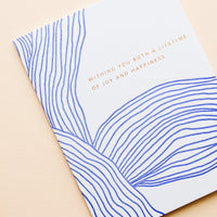 2: Greeting card with wavy cobalt blue line pattern and gold text reading "Wishing you both a lifetime of happiness"