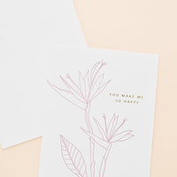 2: Greeting card with pink flower outline drawing and gold text reading "You make me so happy", with white envelope