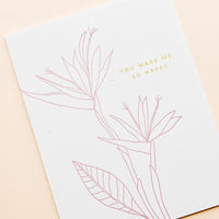 1: Greeting card with pink flower outline drawing and gold text reading "You make me so happy"