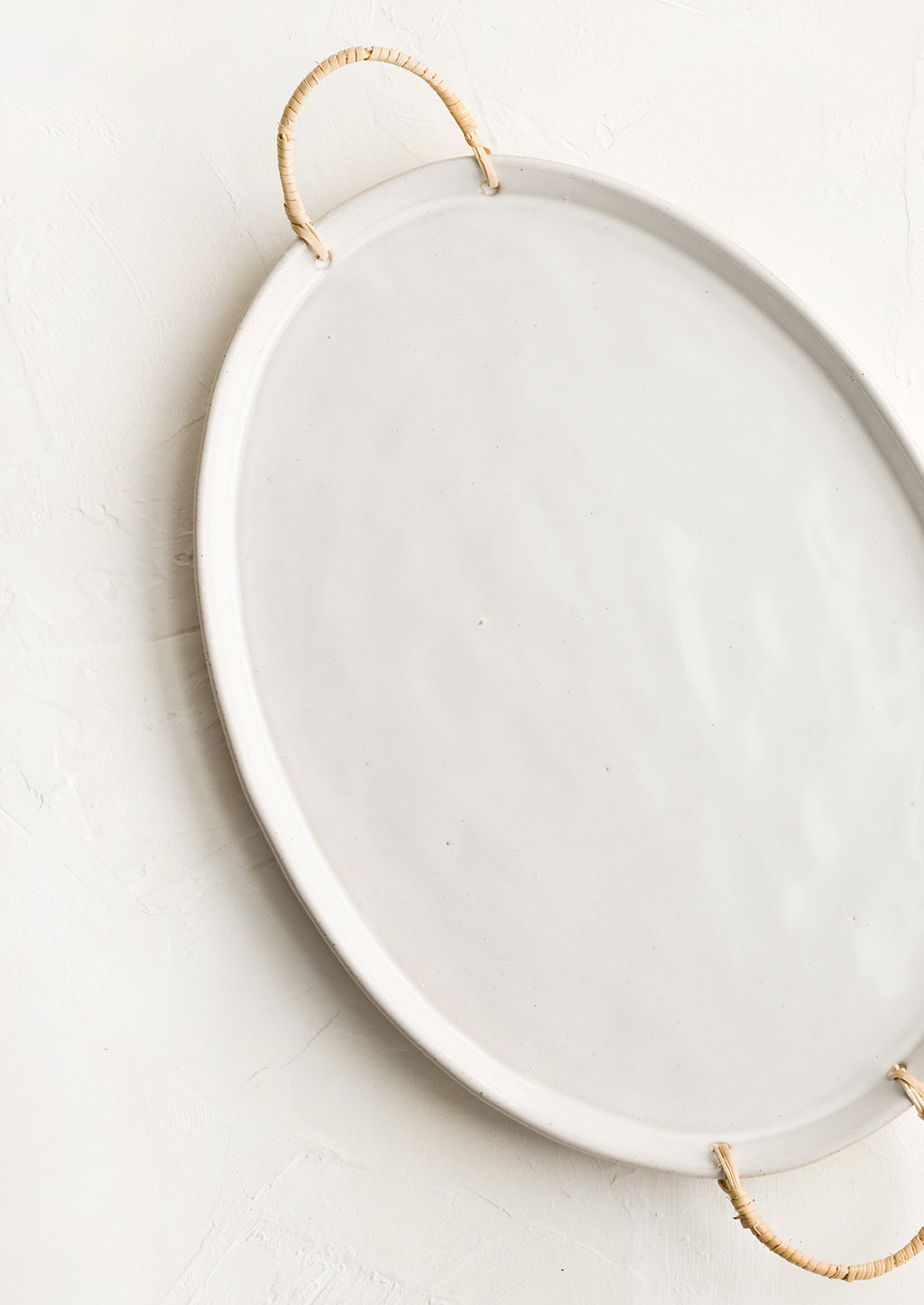 2: A glossy white ceramic platter in oval shape with rattan wrapped handles at sides.