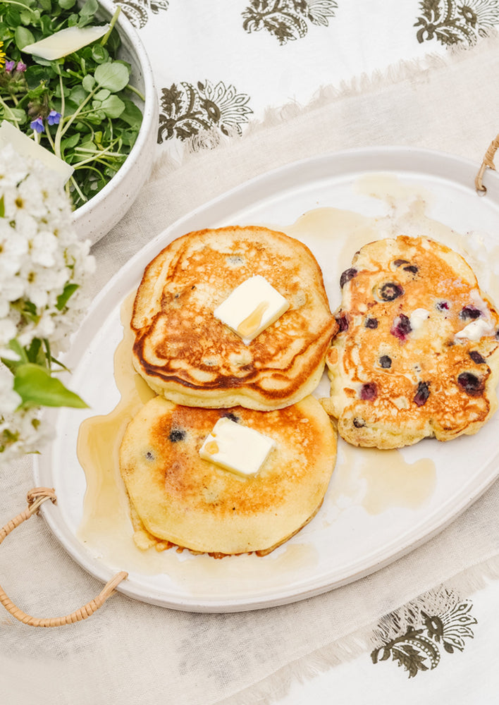 1: A breakfast table setting with pancakes on a ceramic serving platter.