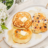 1: A breakfast table setting with pancakes on a ceramic serving platter.