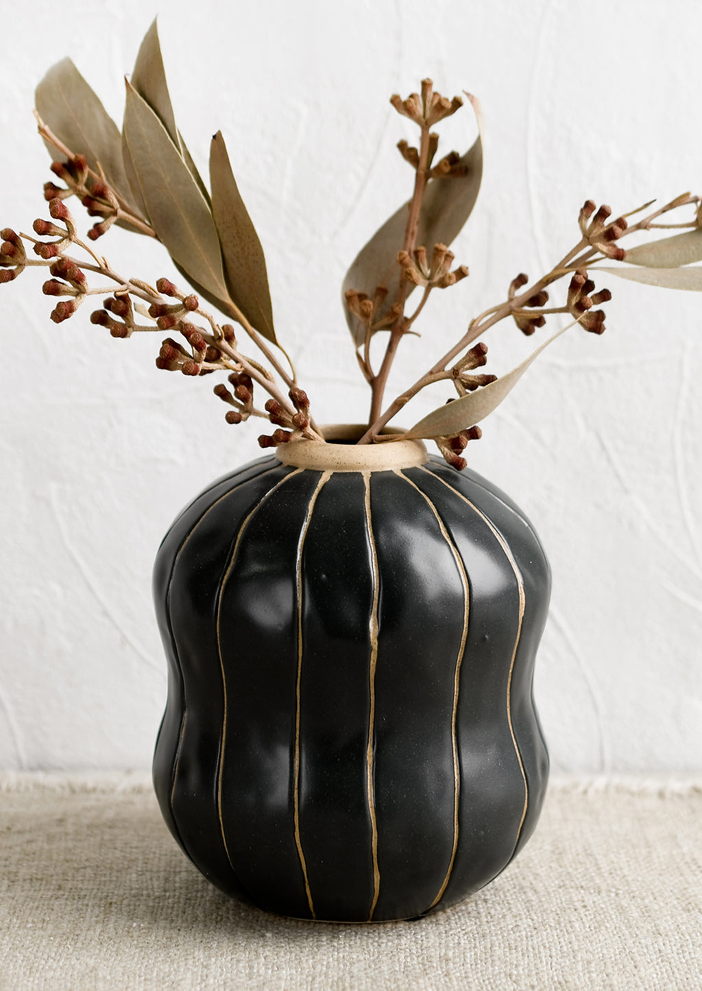 1: A black vase with thin tan vertical stripes, holding dried eucalyptus.