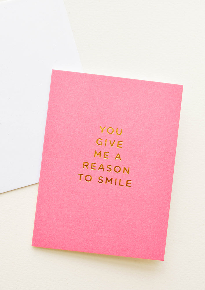 Pink notecard with the text "You Give Me a Reason To Smile" in gold foil.