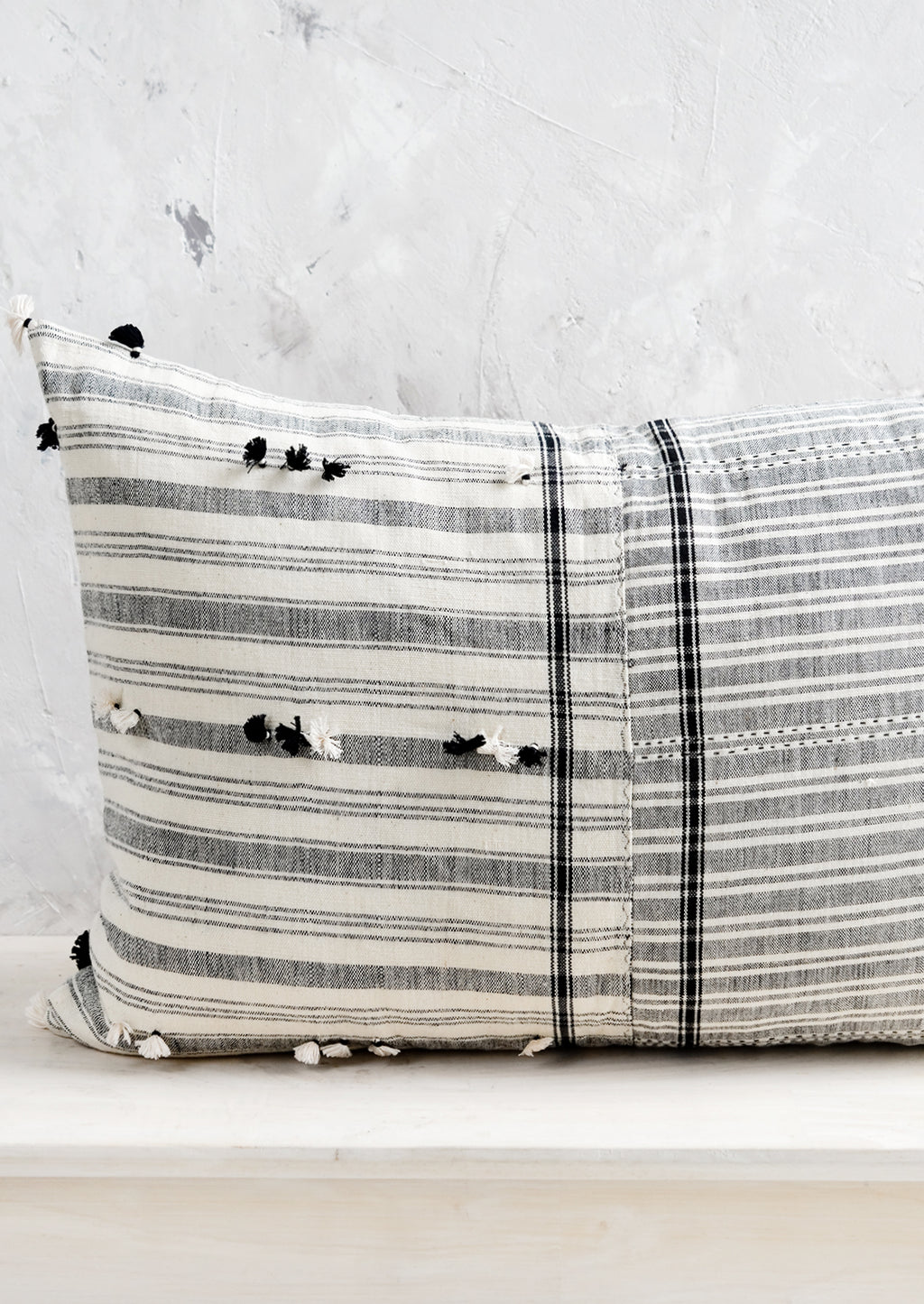 3: A lumbar throw pillow in black and white madras fabric with tassel detailing throughout.