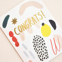 2: Close up of notecard with colorful abstract shapes and the word "Congrats" in gold.
