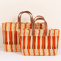 3: An oblong open weave basket in natural reed with bright orange stripes and brown leather handles.