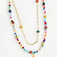 1: Two layered necklace with colorful beaded outer layer and gold chain inner layer.